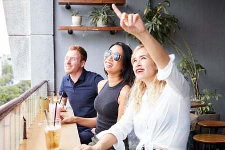 Young people sitting in cafe with drinks and looking at something curious in the sky