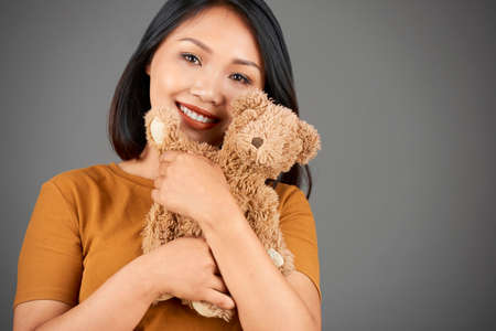 Happy young Asian woman with beautiful toothy smile hugging her little teddy bearの写真素材