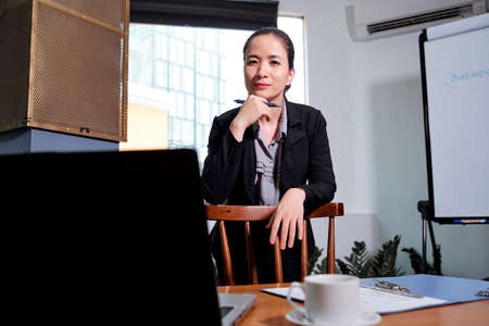 Pretty Vietnamese businesswoman standing at office table and smiling at cameraの写真素材