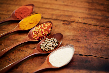 Top view of dried spices on wooden spoons in a row on wooden table in the kitchen