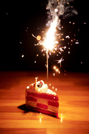Close-up of delicious piece of cake with sparkler on it for birthday party on wooden tableの写真素材