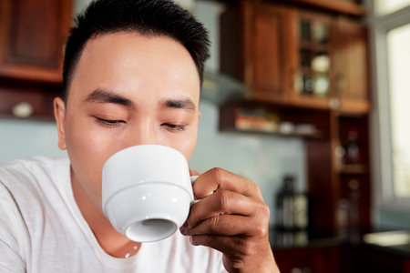 Close-up of young man drinking coffee from cup during breakfast in the morning in the kitchen