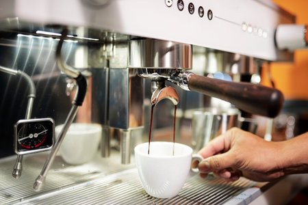 Close-up of barista putting cup under the stream coffee from coffee machine and preparing it for...