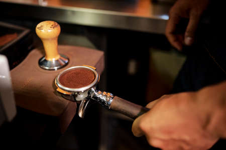 Close-up of barista holding grinder with coffee powder in it made for adding in coffee machineの写真素材