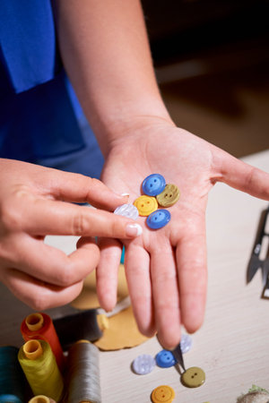 Close-up of dressmaker holding colorful buttons in her hands and choosing one to sew it to the dress