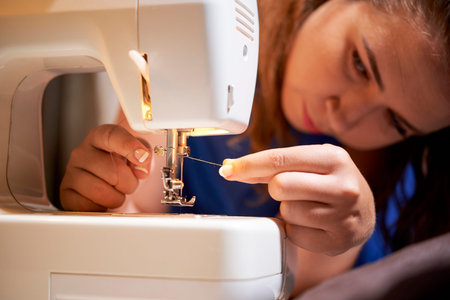 Young seamstress inserting the thread into the needle on sewing machine and is going to sew the new...