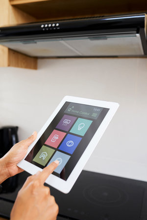 Close-up of housewife setting the temperature on the stove online with digital tablet during cooking...