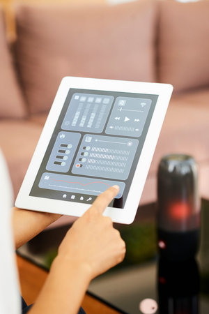 Close-up of woman holding digital tablet and controlling the musical system with online application...