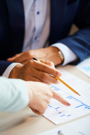 Hands of business executives pointing at document with financial statistics