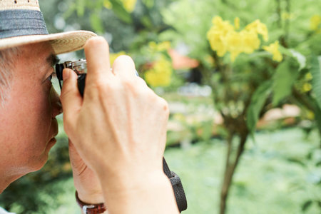 Close-up of senior man in hat photographing the beautiful view of the nature outdoors in summer