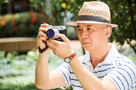 Asian senior man holding digital camera and trying to take a beautiful picture with serious...