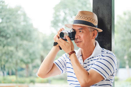 Asian senior tourist in hat photographing the view in beautiful place in summer outdoorsの写真素材