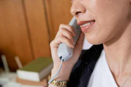 Close-up of businesswoman holding handset and smiling while talking with client at officeの写真素材