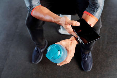 Sportsman resting on gym bench, texting friends and drinking water, view from aboveの写真素材