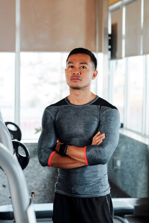 Portrait of young confident fitness instructor standing with his arms folded and looking at camera