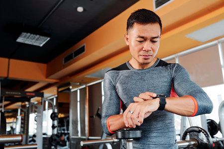 Young fit Asian man checking his pulse on smart watch when working out in gym