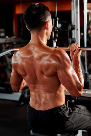 Strong man training upper body in fly machine in gym, view from the backの写真素材