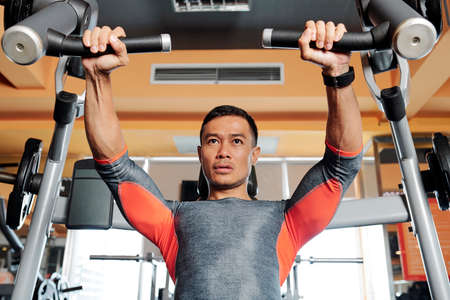 Fit handsome Asian man concentrated on doing chest exercises exercise on fly machineの写真素材
