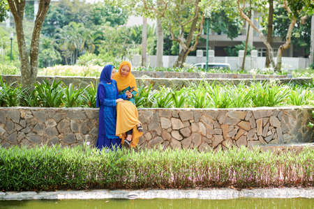 Pretty young Muslim women in bright traditional dresses resting in parkの写真素材