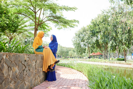 Happy young Asian muslim women in traditional dresses spending sunny day i city parkの写真素材