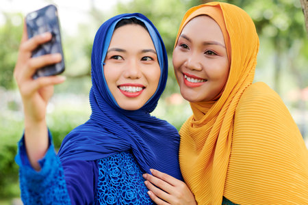 Beautiful young Vietnamese women in hijabs posing for selfie outdoors