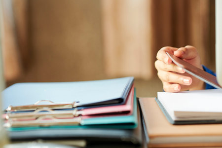 Hand of woman opening planner on her desk with clipboards and booksの写真素材