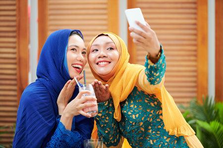 Beautiful young Vietnamse women in hijabs posing for selfie outdoors