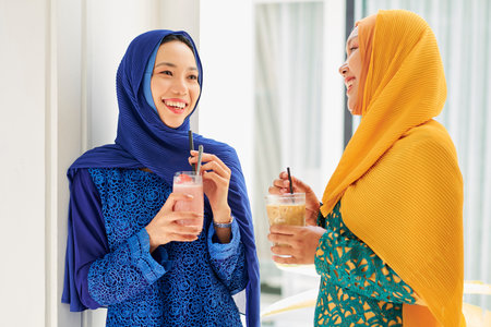 Beautiful young Asian women in hijabs drinking smoothie and discussing news