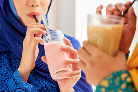 Glasses with delicious fruit smoothie in hands of young muslim womenの写真素材