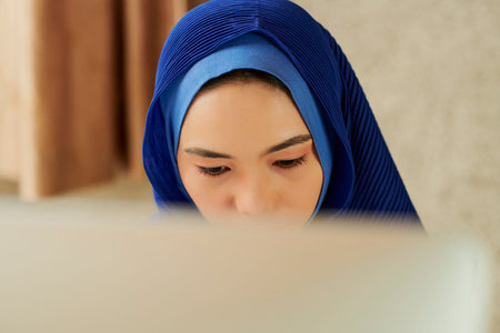 Concentrated young woman hijab reading information on computer screen when working in officeの写真素材