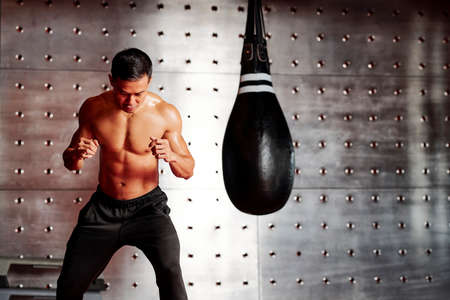 Shirtless muscular boxer warming up with punching bag before fight in gymの写真素材