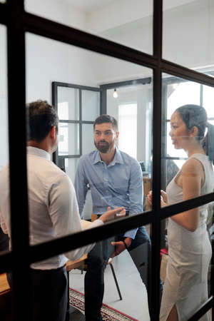 Group of young business people standing behind the glass wall at office and discussing business togetherの写真素材