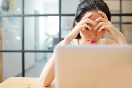 Asian young businesswoman sitting at the table in front of laptop computer and concentrating on her...