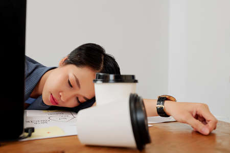 Young exhausted businesswoman lying on the table and sleeping in front of laptop computer she tired after hard work at officeの写真素材