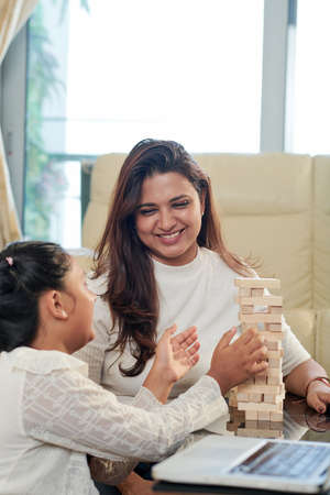 Happy mother playing Jenga with her daughter they sitting at the table and having fun at homeの写真素材