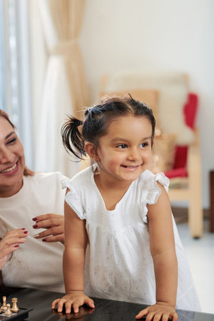 Cute smiling little girl playing together with her mother at home