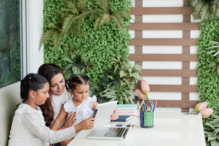 Mother with her two children sitting at the table and watching something together on digital tablet