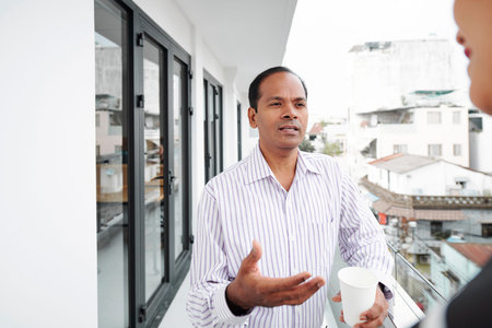 Indian mature businessman standing and talking to his colleague at balcony during coffee break