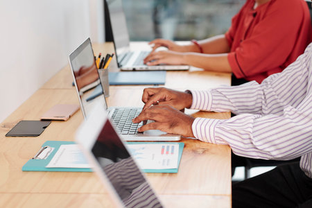 Close-up of business people sitting at their workplaces and working online typing on laptop computers at officeの写真素材