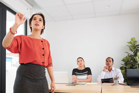 Indian young businesswoman pointing at something and holding business presentation for her...
