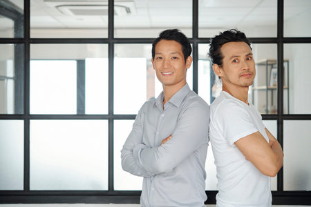 Confident cheerful Vietnamese business people standing back to back and smiling at camera