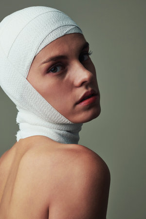 Serious beautiful young woman with head bandage after accident turning back and looking at camera