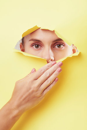 Young woman tearing bright yellow paper and looking at camera