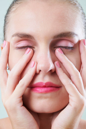 Pretty woman with pink make-up touching her face with manicured hands
