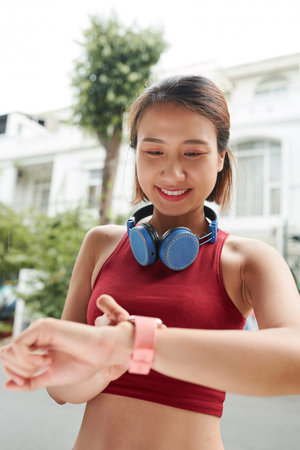 Positive pretty young Vietnamese woman checking notifications on her smart watch