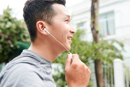 Happy young Asian man listening to music in earphones when jogging outdoors