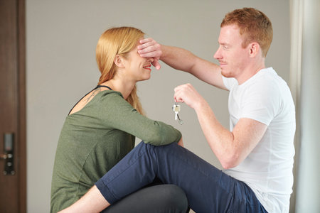 Handsome young man making surprise for girlfriend, covering her eyes and giving apartment keys
