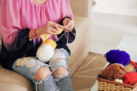 Hands of senior woman knitting white and yellow wool scarf for winterの写真素材