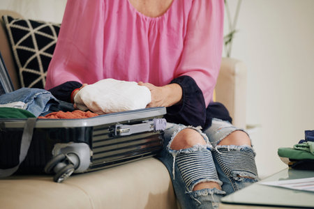Close-up image of woman sitting on sofa and unpacking suitcase after trip