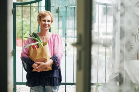 Portrait of happy senior woman standing outdoors with big bag of fresh groceriesの写真素材